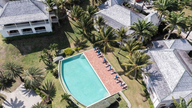 Vue aérienne d’un complexe hôtelier doté d’une piscine entourée de palmiers et de chaises longues.