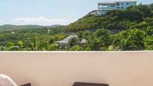 Un balcon doté de meubles en osier et offrant une vue sur une colline où se trouve un bâtiment.