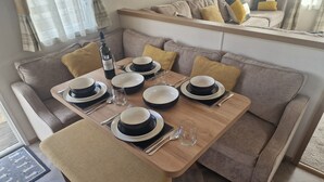 A dining area with a wooden table set for four, a bottle of wine, and a sofa in the background. - Shadow Escapes, Shadow Escapes - Morning Rising (Ladybank)