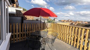 Een balkon met een rode parasol, een houten schutting en een tafel met stoelen.