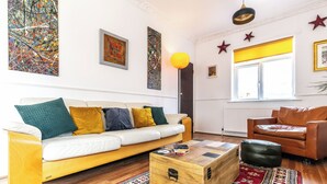 Een woonkamer met een witte bank, een houten salontafel, een kamerkleed met een patroon en een raam met stersieraden.