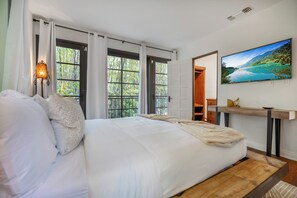 A bedroom with a large bed, a nightstand with a lamp, a wooden bench, a desk with a chair, and a painting on the wall. - Sunset Vale (West Hollywood)