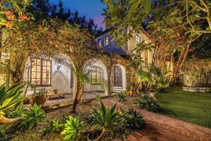 A courtyard with a brick pathway, potted plants, and a building with arched windows. - Sunset Vale (West Hollywood)