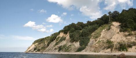 A coastal landscape with a sandy beach, a rocky cliff with vegetation, and a calm sea.