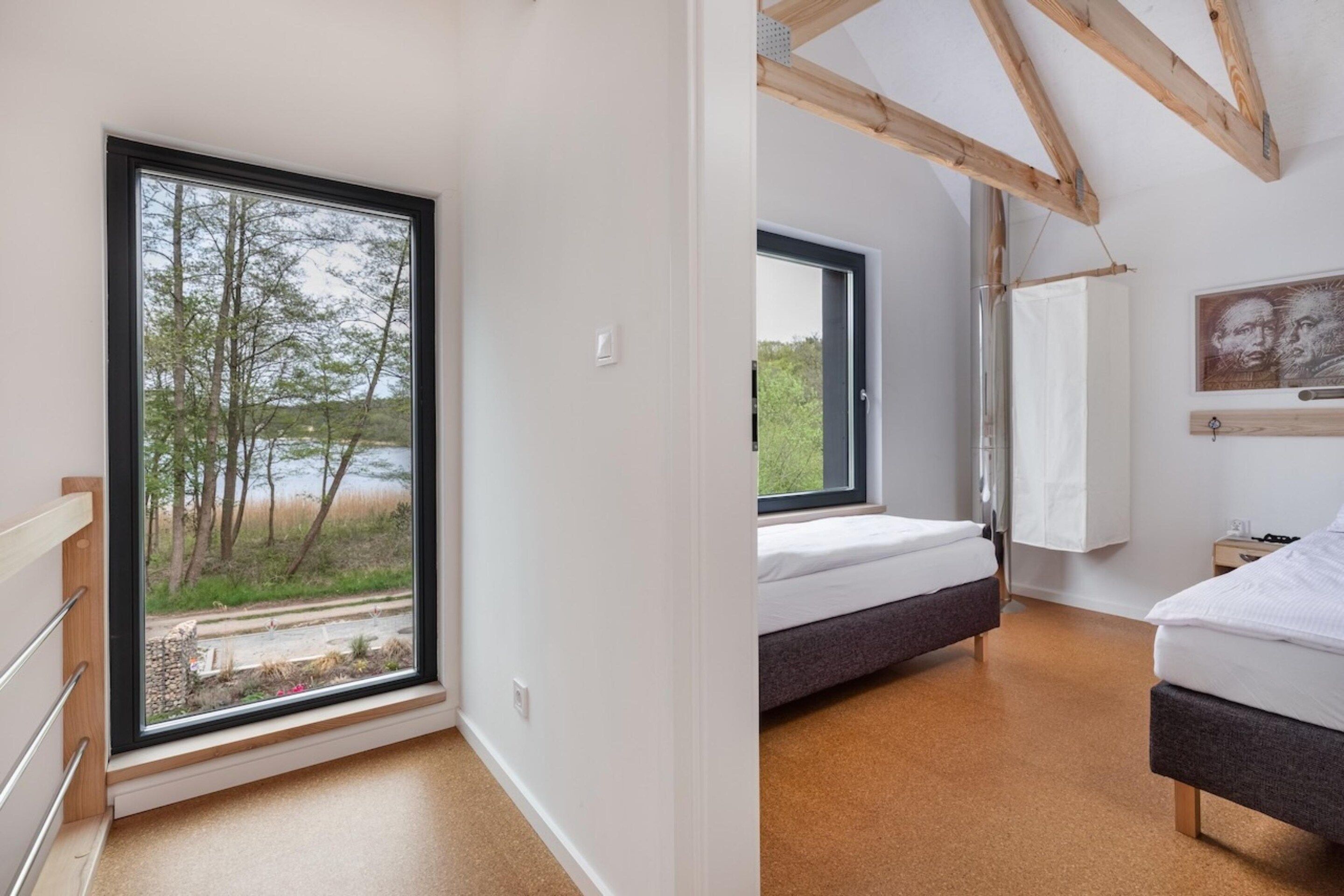 A bedroom with a large window, a bed, and a view of trees and a body of water.