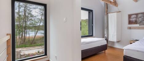 A bedroom with a large window, a bed, and a view of trees and a body of water.