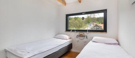 A bedroom with two single beds, a window with a view of a house, and a wooden ceiling beam.