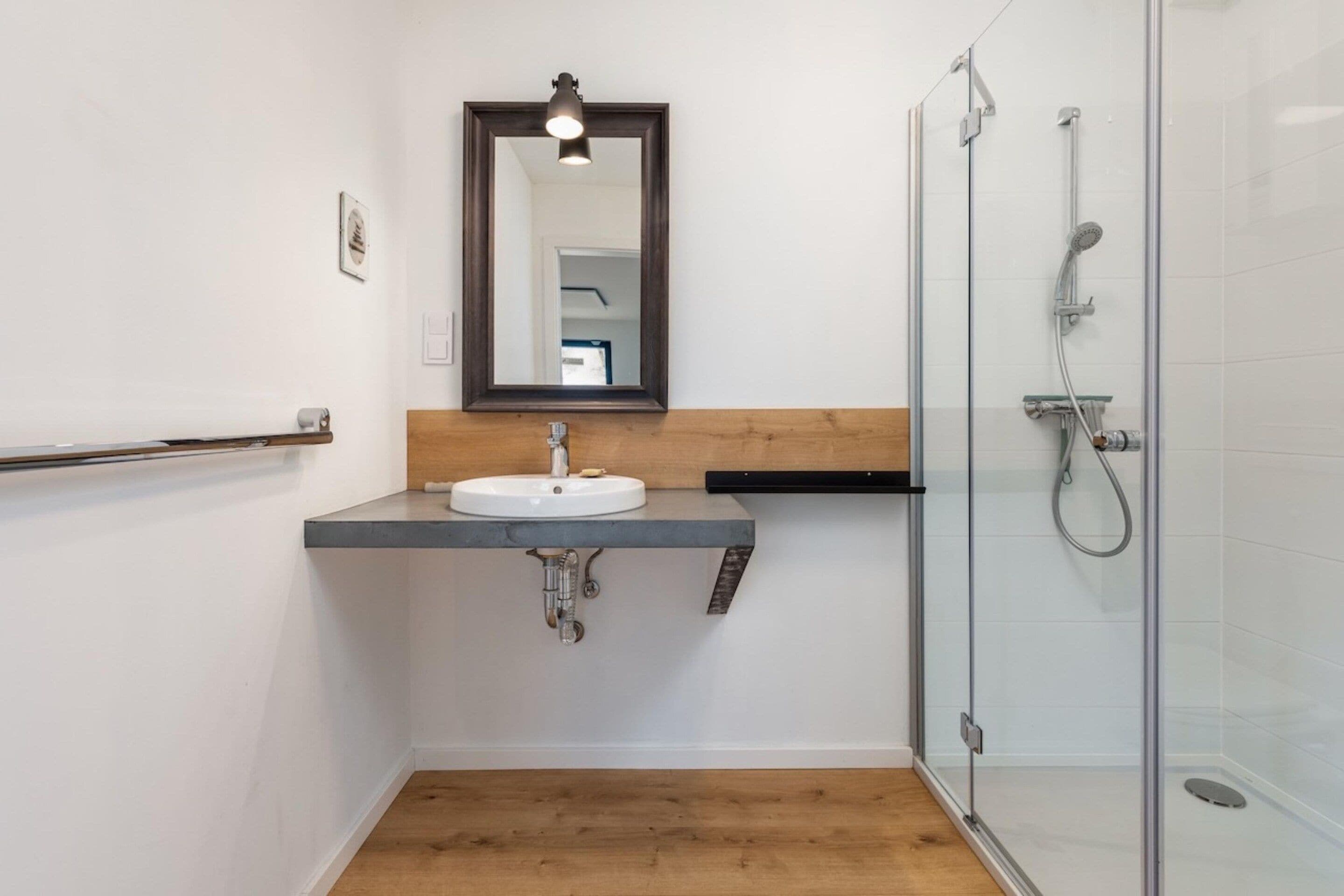 A bathroom with a white sink, a wooden countertop, a mirror, and a glass shower enclosure.