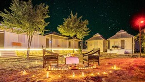 A nighttime outdoor setting with tents and a dining area with chairs and a table, surrounded by candles. - Desert Stay Camping Jaisalmer (Jaisalmer)