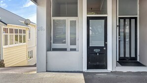 A building with a black door, a window with a white frame, and a number '86B' on the wall. - Stanley Bay Apartment, Devonport (Stanley Point)
