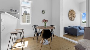 A modern living room with a round wooden table, black chairs, a blue sofa, and a decorative wall piece. - Stanley Bay Apartment, Devonport (Stanley Point)