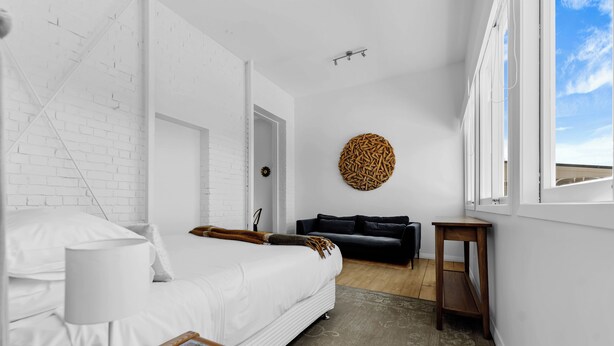 A modern hotel room with a white brick wall, a round wooden wall art piece, a black sofa, and a wooden side table. - Stanley Bay Apartment, Devonport (Stanley Point)
