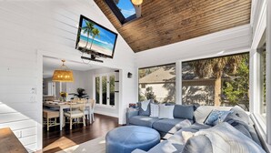 A modern living room with a large sectional sofa, a round ottoman, and a television mounted on the ceiling.