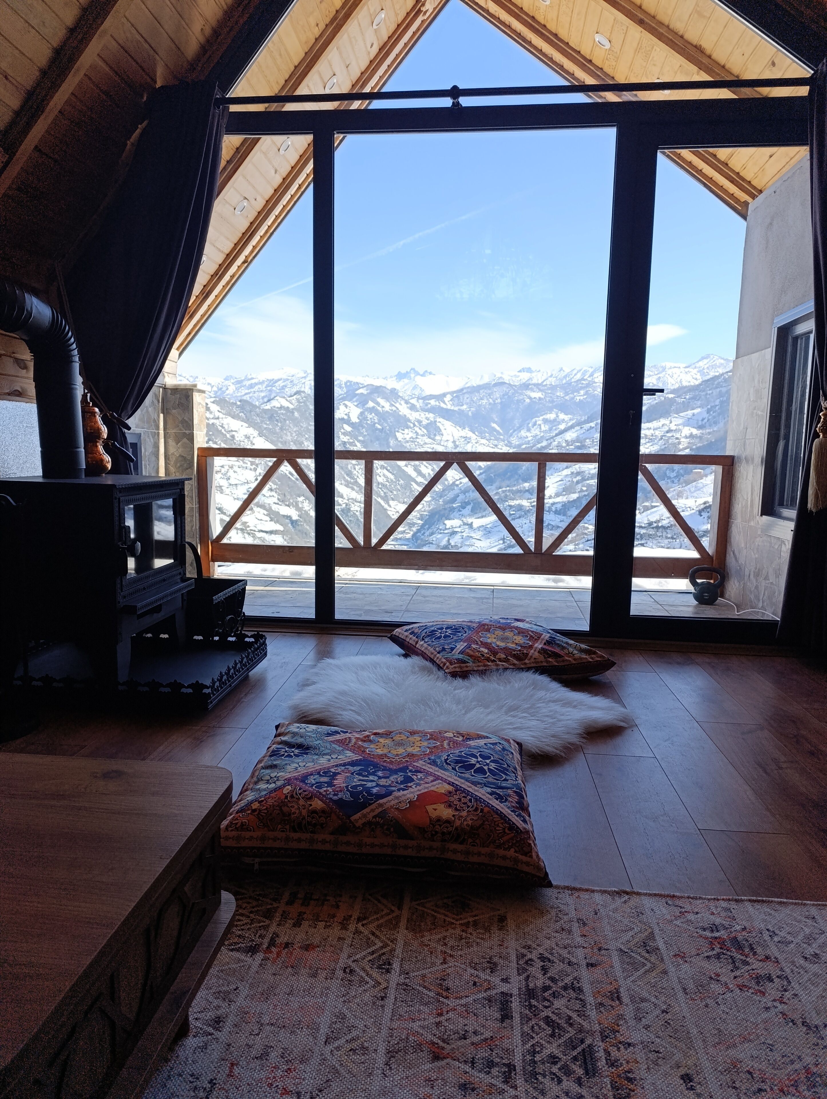 Ein gemütliches Zimmer mit Holzboden, Kamin und großem Fenster mit Blick auf die Berge.