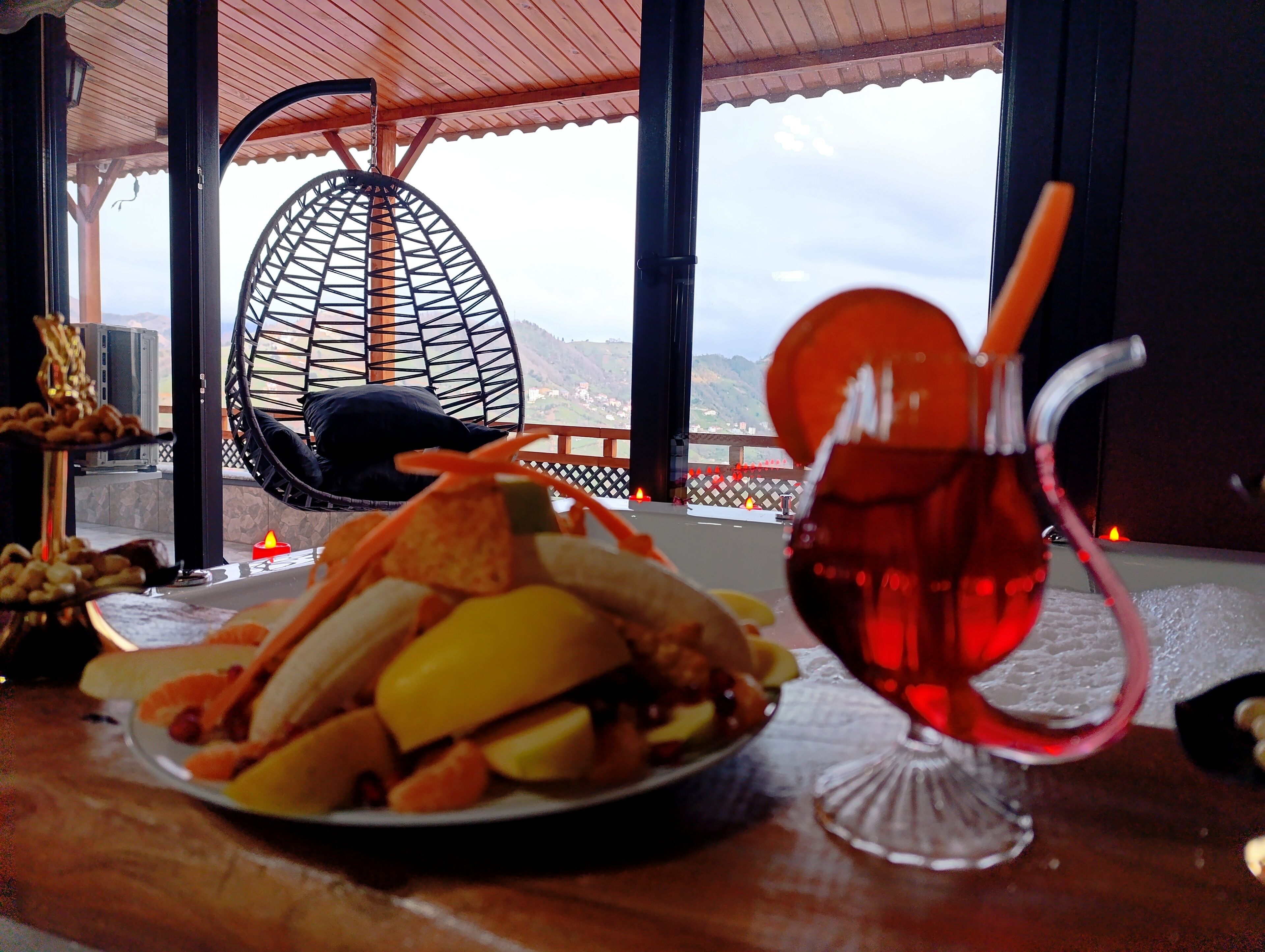 A dining table with a plate of food, a glass of red drink, and a hanging chair.