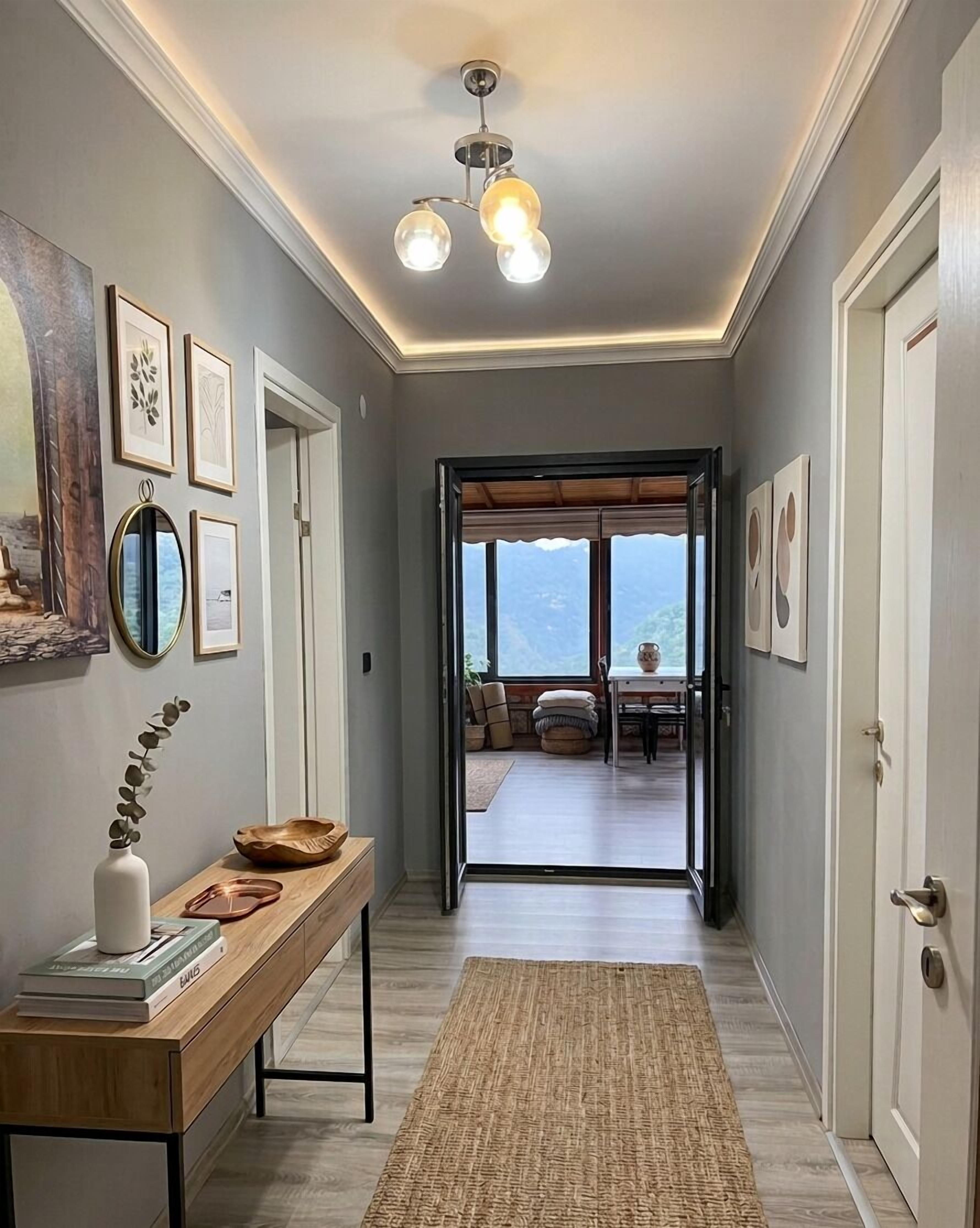 A hallway with a wooden bench, framed artwork, and a view into a dining area with a table and chairs.