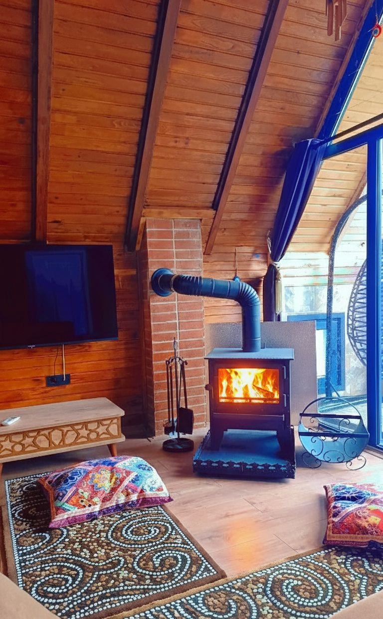 Una habitación acogedora con una estufa de leña, un televisor en la pared y un amplio ventanal que proporciona luz natural.