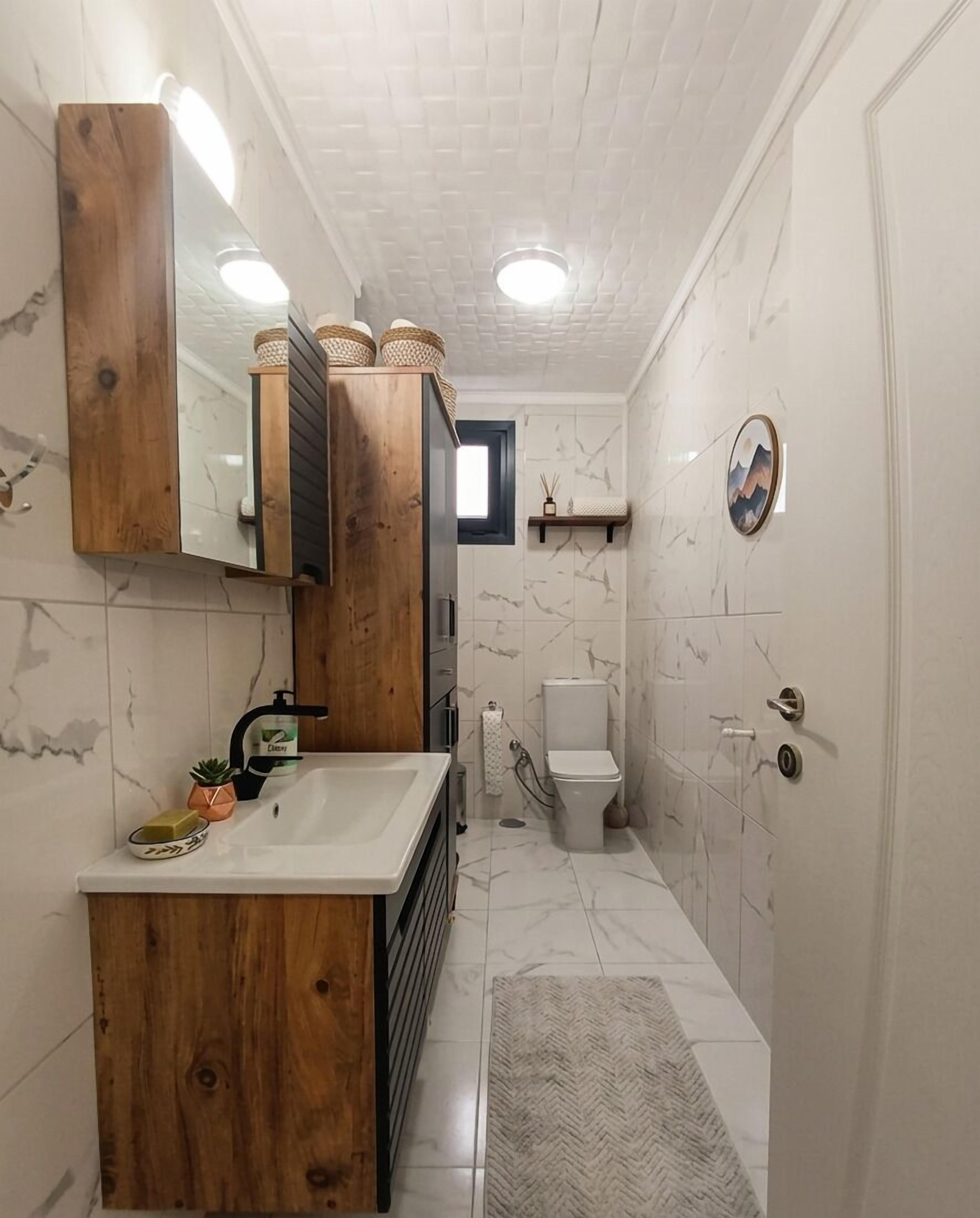 A bathroom with a wooden vanity, a white sink, a toilet, and a shower area.