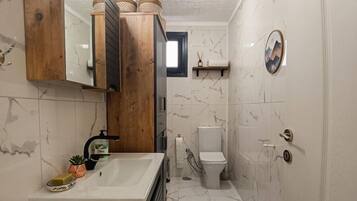 A bathroom with a wooden vanity, a white sink, a toilet, and a shower area.