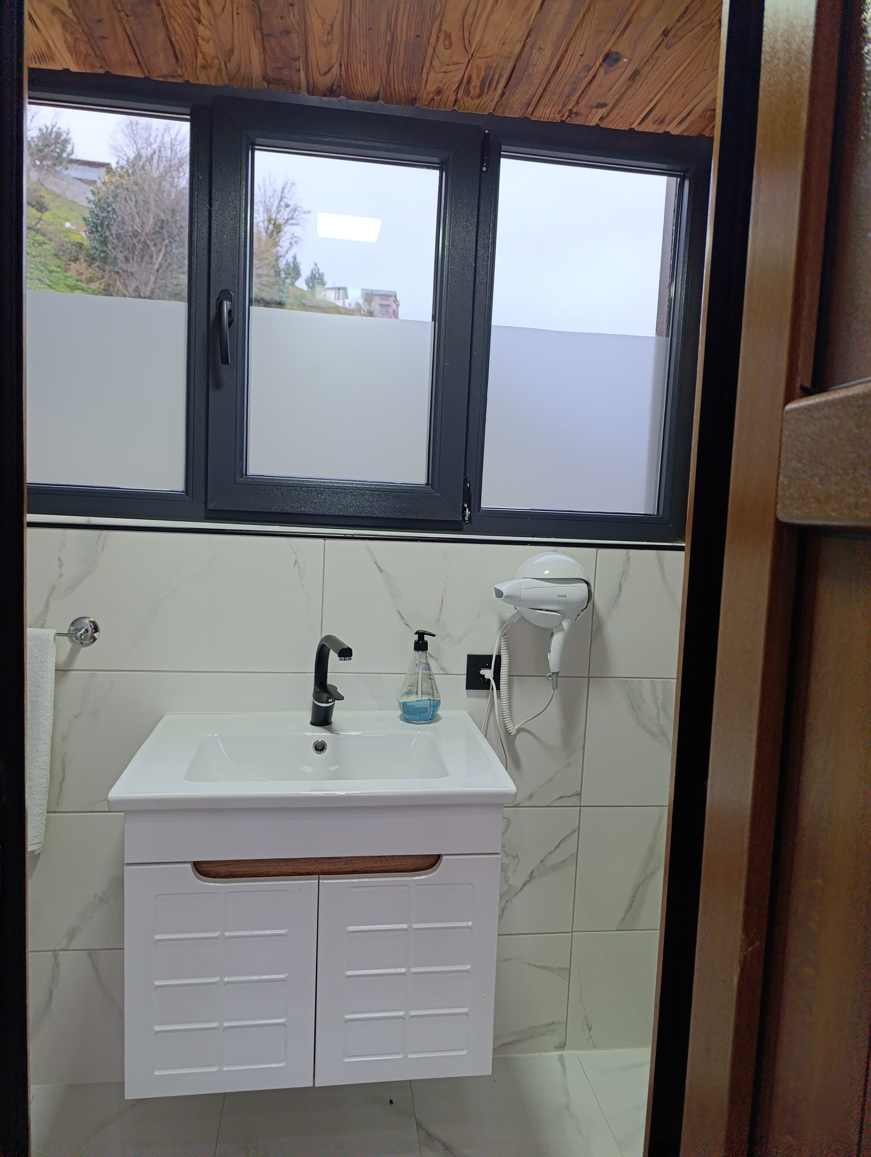 Un baño con lavamanos blanco, grifo negro y un secador de pelo en la pared.