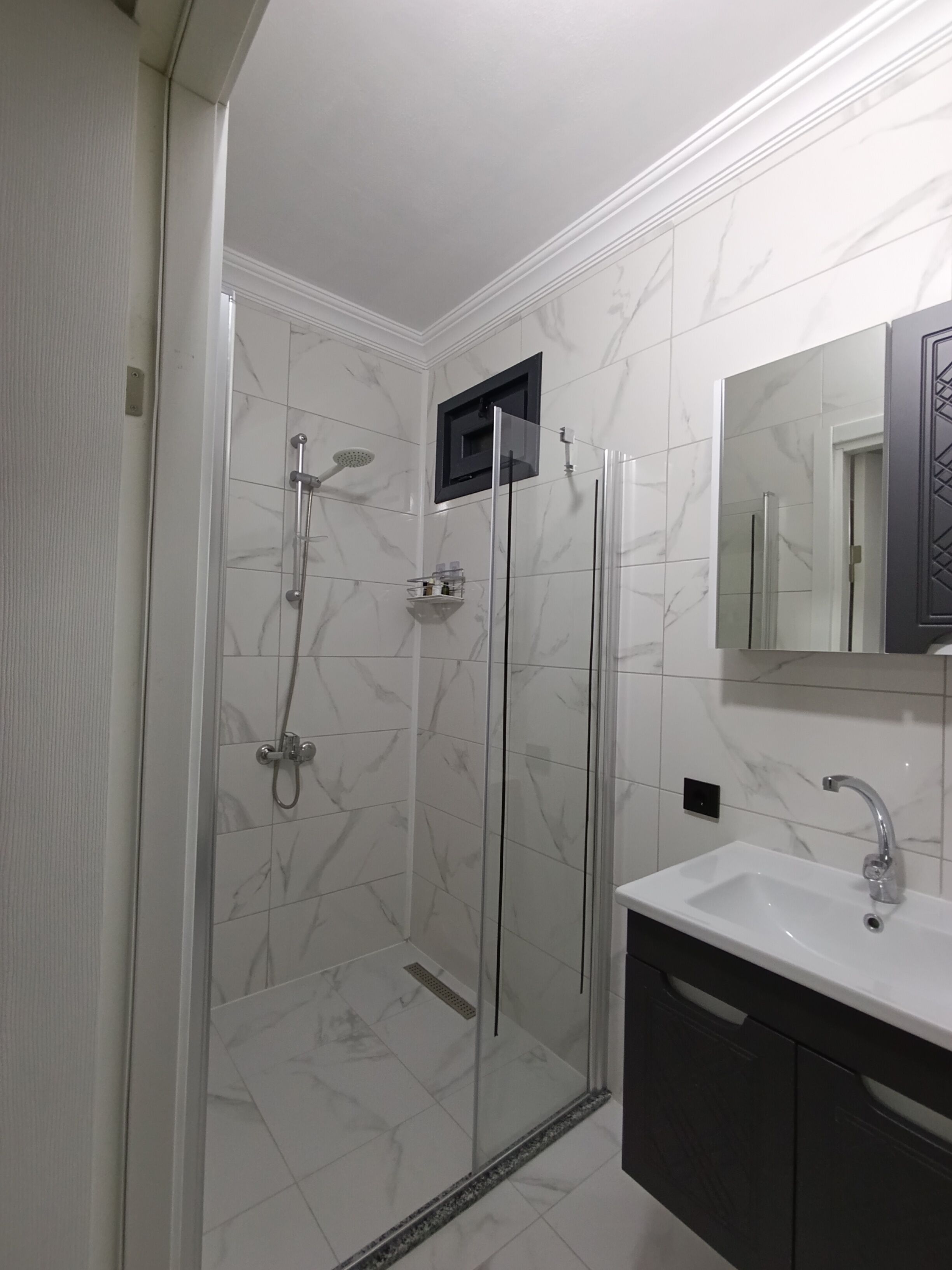 A modern bathroom with a glass-enclosed shower, a white sink, and a dark-toned vanity.