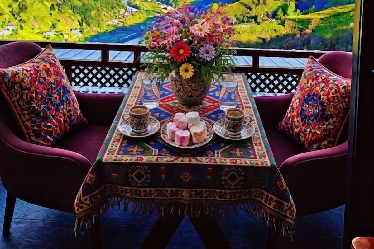 A balcony with a table set for two, a vase of flowers, and a view of a mountainous landscape.