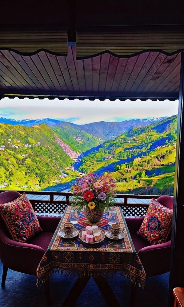 Un balcon avec une table dressée pour deux personnes, un vase de fleurs et une vue sur un paysage montagneux.