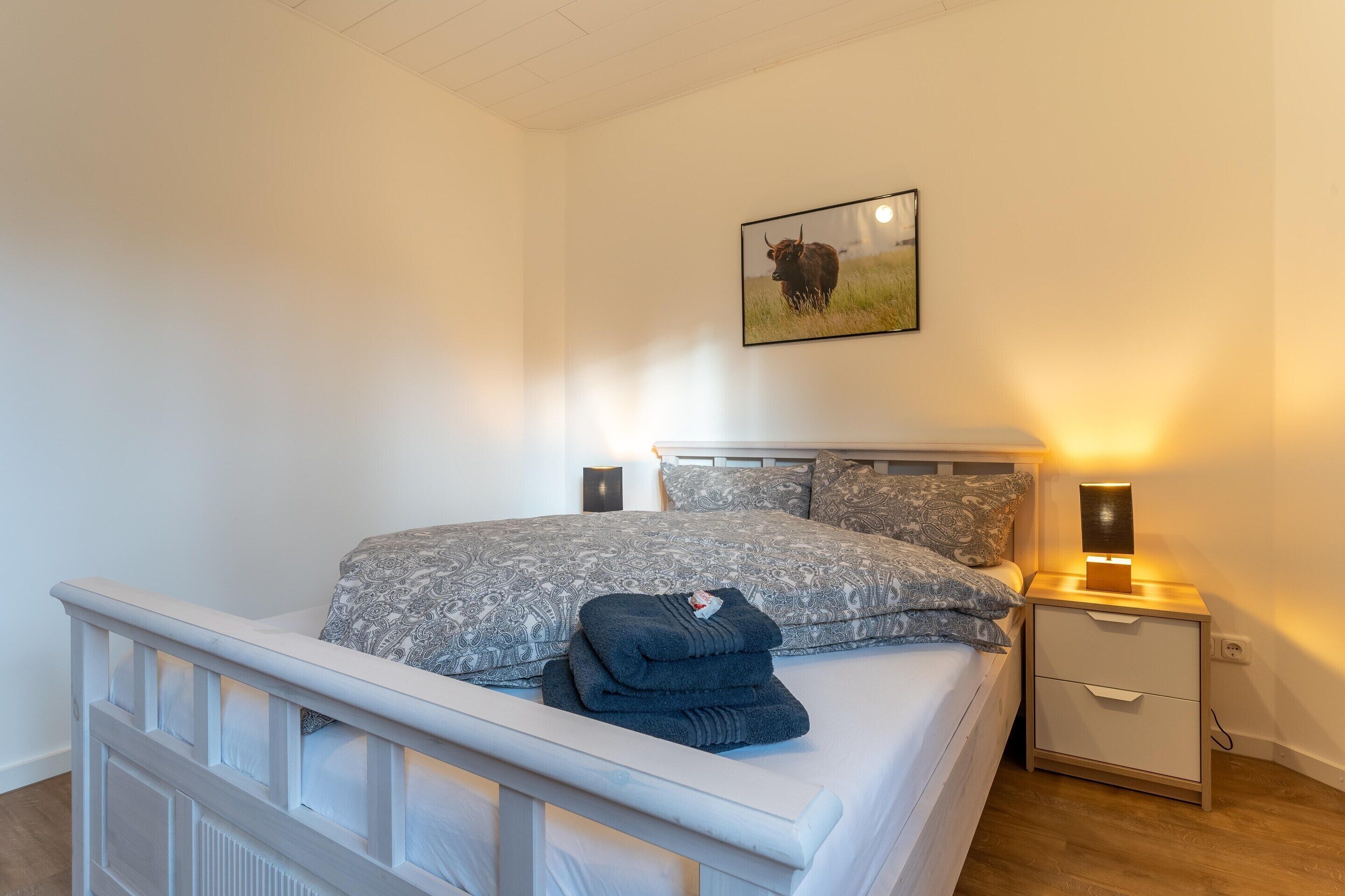 Quarto com cama, mesas de cabeceira e um quadro na parede.