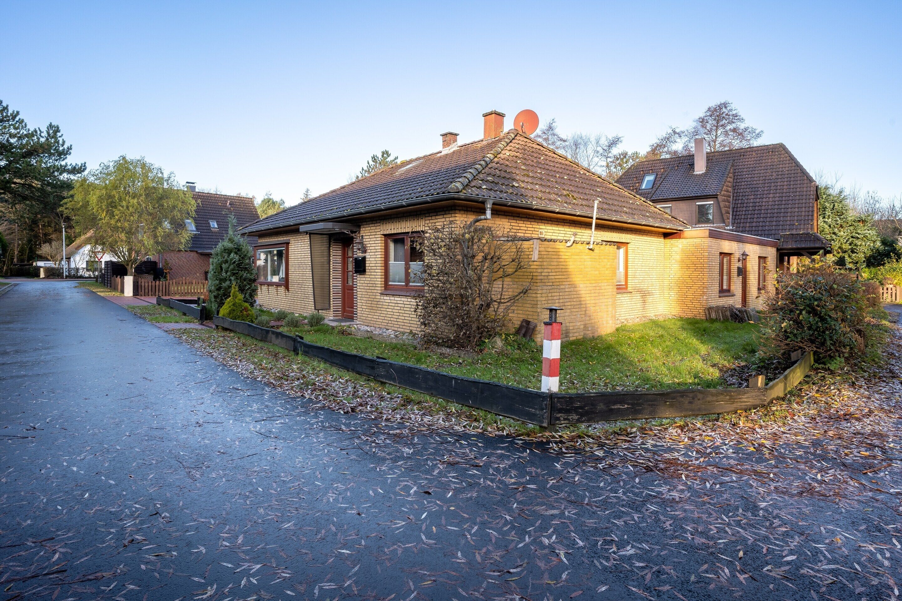 A two-story brick house with a sloped roof, a satellite dish, and a small front yard with a fence.