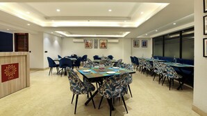 A conference room with multiple tables and chairs, a reception desk, and framed pictures on the walls. - OPO Essential Sec 21 (Gurugram)