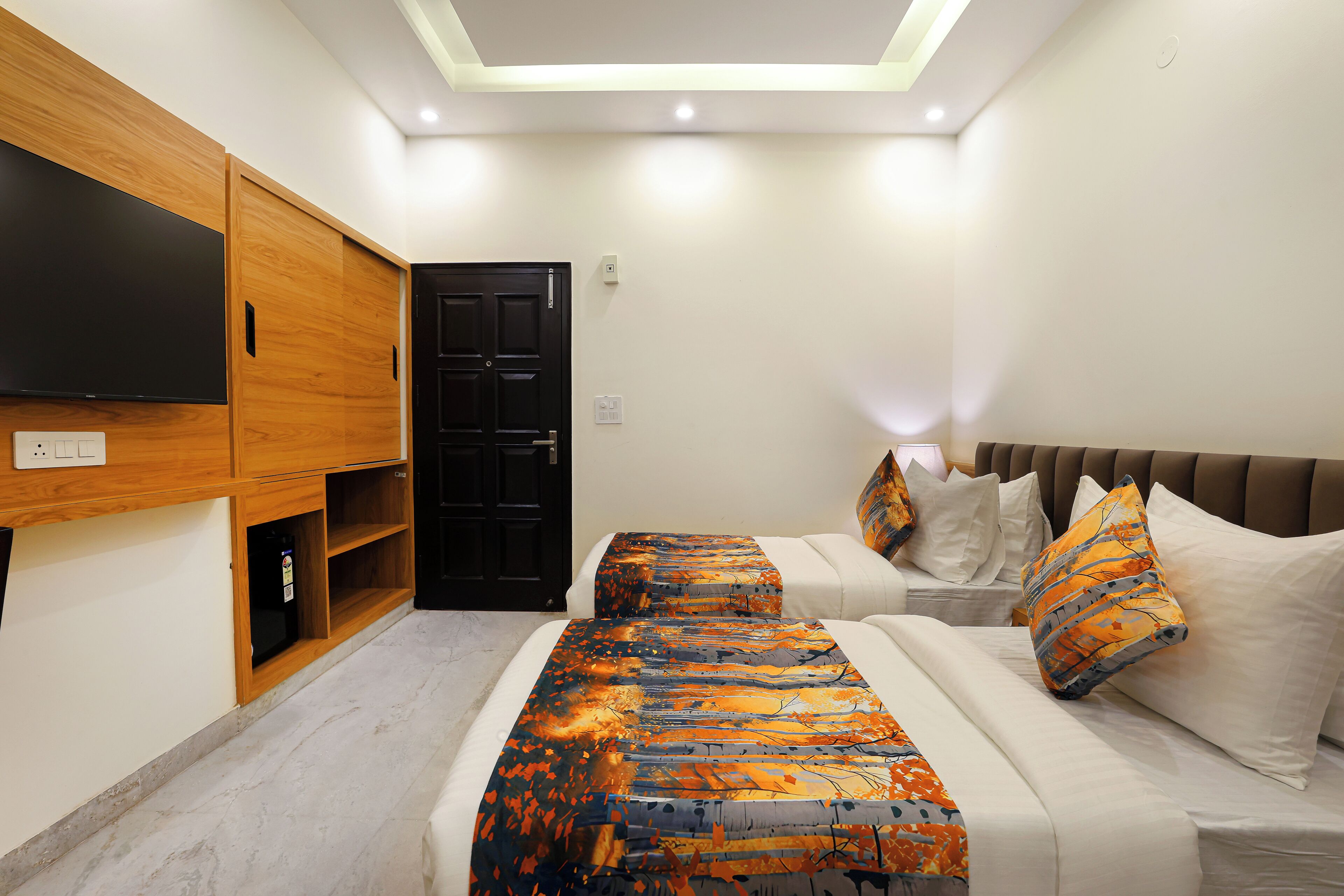 A bedroom with a bed, a TV mounted on a wooden cabinet, a door, and a ceiling light.
