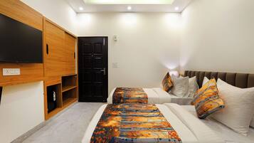 A bedroom with a bed, a TV mounted on a wooden cabinet, a door, and a ceiling light.