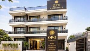 A modern multi-story building with a sign indicating it offers rooms, a restaurant, conference, and banquet services. - OPO Essential Sec 21 (Gurugram)