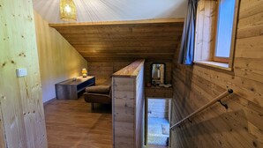 Een houten interieur met een trap naar een vide, een klein tafeltje met een lamp en een raam met gordijnen.