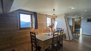 Een eetgedeelte met een houten tafel en stoelen, een vaas met bloemen en uitzicht op het landschap door een raam.