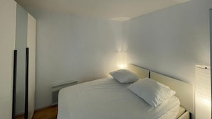 Un dormitorio con cama, mesita de noche, lámpara de pared y radiador.