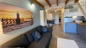 Un espacio acogedor con un sofá y un cuadro de un faro. Cuenta con una cocina equipada con electrodomésticos modernos y un comedor con mesa y sillas.