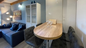 Una sala de estar moderna con una mesa de comedor de madera, dos sillas negras con acolchado, un sofá gris con cojines azules, un armario blanco y un cuadro de un faro.