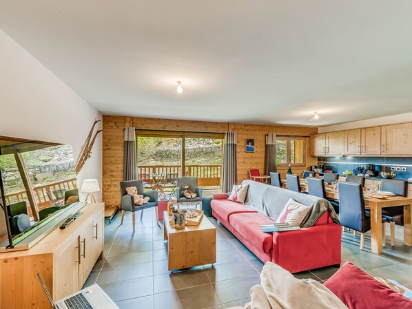 A cozy living room with a sofa, chairs, a coffee table, and a TV. There's a kitchen area with cabinets and a dining table. - 4* Apartment in Tignes - Ski-in/Ski-out, Hotel Services Included (Tignes)
