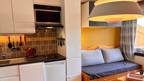 Una cocina compacta con microondas, estufa y lavamanos, un comedor con una mesa dispuesta para dos personas, y una zona de descanso acogedora con cama y almohadas.