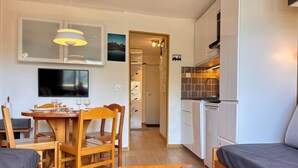 Un espacio habitable compacto con zona de comedor, kitchenette y televisor montado en la pared.