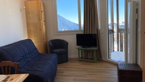 A cozy room with a blue sofa, a small armchair, a television on a green stand, and a wooden cabinet.