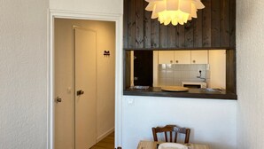 A compact kitchen with a wooden ceiling, a dining area with a table and chairs, and a door leading to another room.
