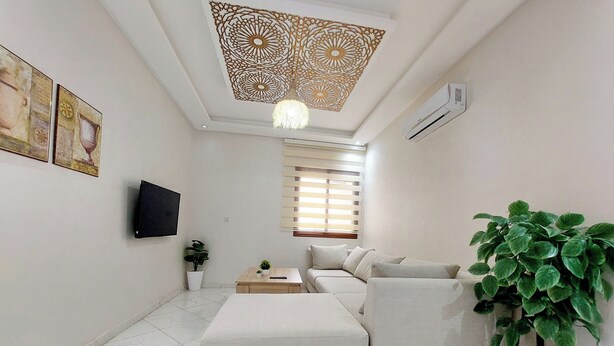 Una sala de estar moderna con un sofá, una mesa de centro, un televisor montado en la pared, una planta en maceta y un panel decorativo en el techo.