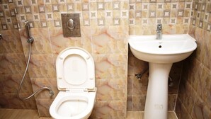 A bathroom with a toilet and a sink, both with white fixtures, and a showerhead. - Hotel Jaypee Inn By GRB (Howrah)