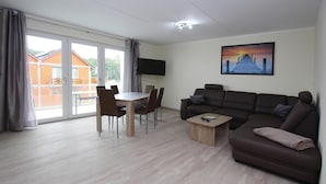 A spacious living room with a large sofa, a dining table with chairs, a flat-screen TV mounted on the wall, and a painting above the sofa. - Appartement Hafenflair am Plauer See (Plau am See)