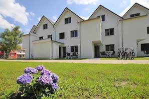 A row of white buildings with multiple windows and doors, a grassy area in the foreground, and bicycles parked outside.