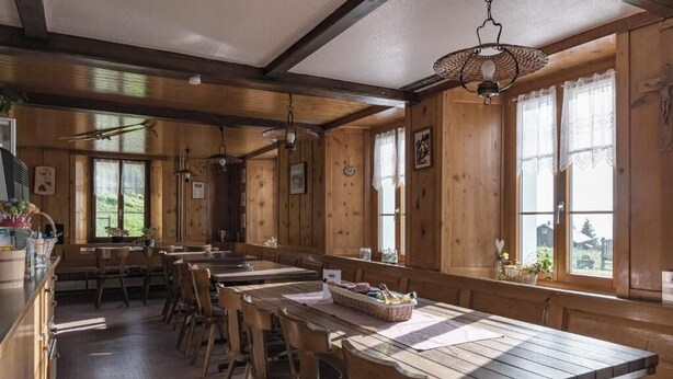 A wooden interior with long tables and benches, large windows, and hanging light fixtures. - Berggasthaus Rigi Burggeist (Gersau)