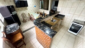 A kitchen with a granite countertop, a sink, a stove, and a dining area with chairs and a table. - Pousada da Praia Frade (Angra dos Reis)