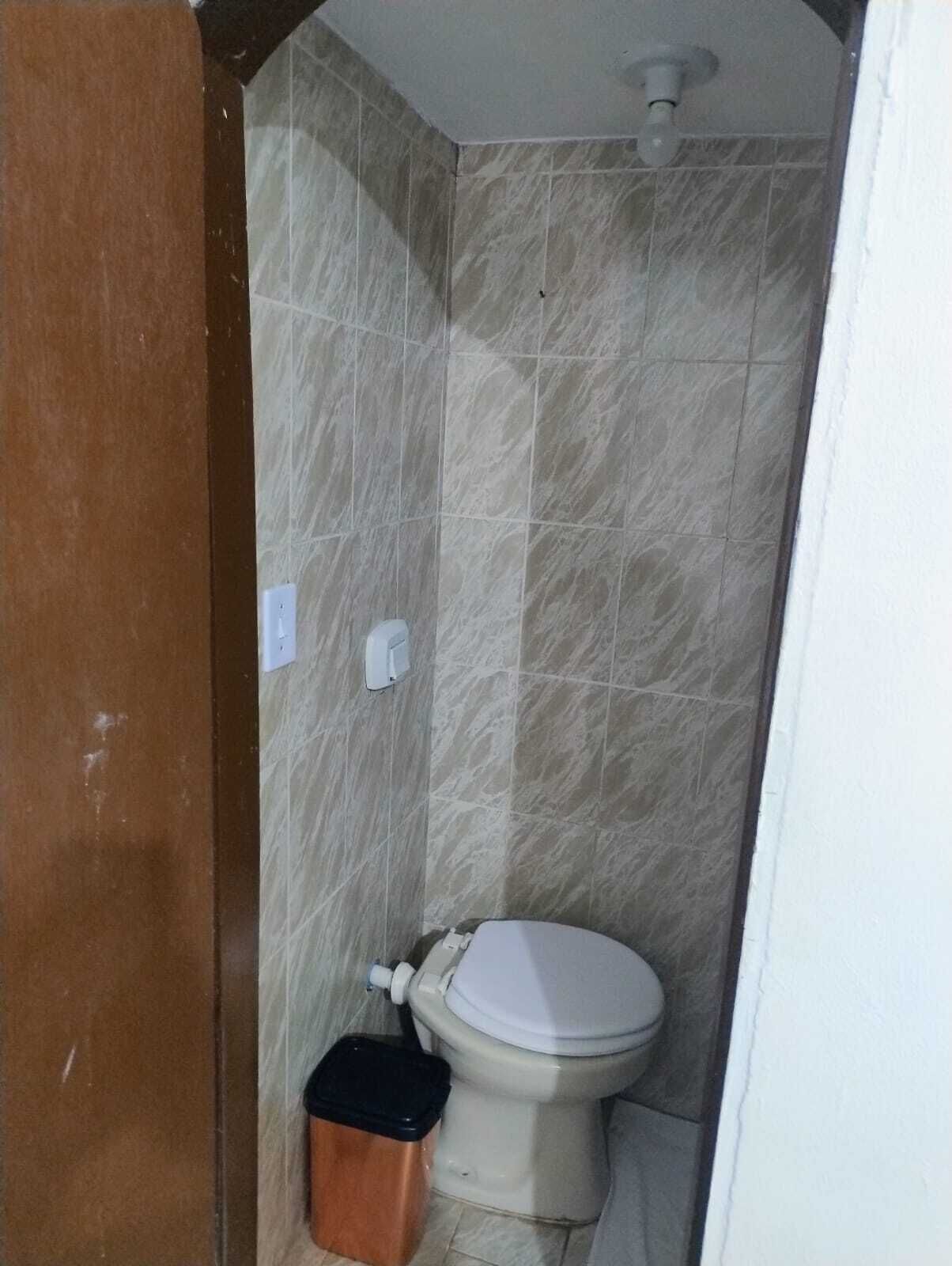 Een kleine badkamer met toilet, een prullenbak en een wandlamp.